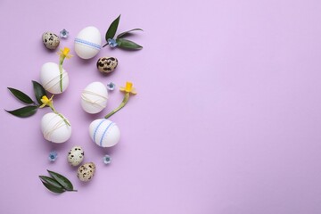 Fototapeta na wymiar Festively decorated Easter eggs and green leaves on lilac background, flat lay. Space for text