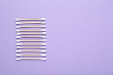 Wooden cotton buds on violet background, flat lay. Space for text