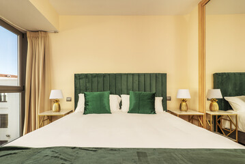 bedroom with a double bed with green cushions and upholstered headboard of the same color next to a window