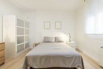 bedroom with a double bed with gray cushions and a white wooden headboard, different bedside tables...