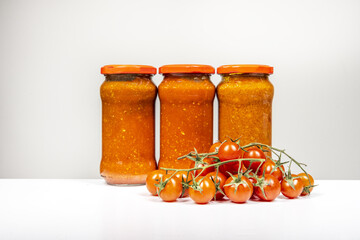 Still life with glass jars of canned red tomato sauce for pasta with a string of fresh cherry tomatoes