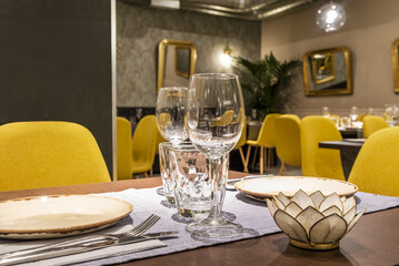 Tables in the dining room of a restaurant with a service set up with crockery and porcelain glasses and crystal goblets, decorative elements and mirrors with gold frames