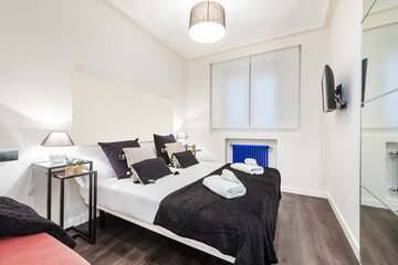 Bedroom with sofa, many cushions, windows with shutters, blue radiator and wood-like stoneware...