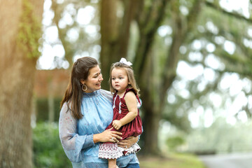 A beautiful brunette mother holding her baby toddler daughter outside in the fall.