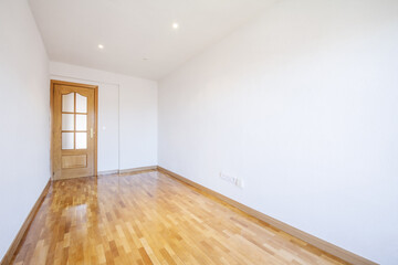 Empty room with polished oak parquet floors, oak skirting boards and doors and white walls
