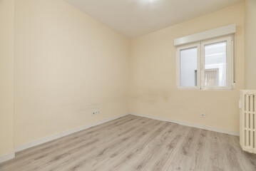 Empty living room with cast iron radiator with white aluminum window and cream colored walls