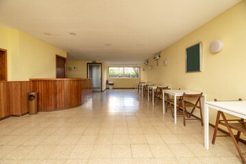 Large community room in a building with white wooden tables with folding chairs, a wooden counter and windows to a garden area