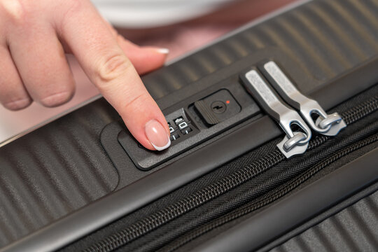 Fingering the numbers on the combination lock of the suitcase to open it