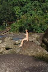 Young and sexy woman stand on rock wearing swimsuit on the beautiful river in the jungle