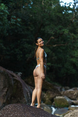 Fototapeta na wymiar Young and sexy woman stand on rock wearing swimsuit on the beautiful river in the jungle