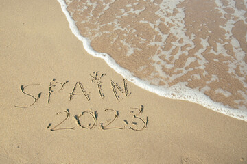 Spain 2023, lettering on the beach with wave and clear blue sea. 