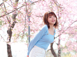 Outdoor portrait of beautiful young Chinese girl posing with blossom cherry tree brunch background in spring garden, beauty, summer, emotion, lifestyle, expression and people concept.
