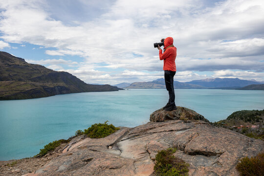 person in red jacket on top of a hill taking photo of the landscape, nature photographer, Patagonia, Chile - Powered by Adobe