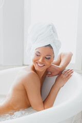 Happy beautiful white woman with towel over her head smiling while lying in bubble bath