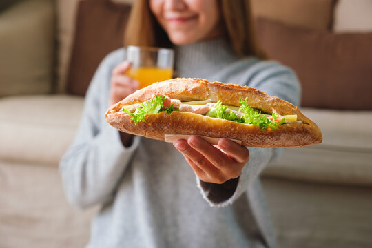 Blurred image of a young woman holding and eating french baguette sandwich and orange juice at home