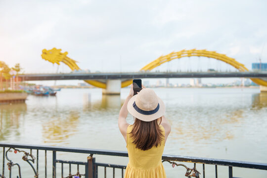 Woman Traveler with yellow dress visiting in Da Nang. Tourist sightseeing the river view with Dragon bridge at love lock bridge. Landmark and popular. Vietnam and Southeast Asia travel concept