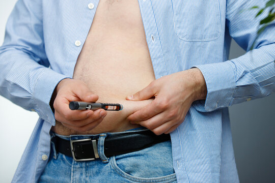 Cropped photo of a man in jeans and t-shirt with syringe making insulin injection to himself in abdomen, diabetes concept.