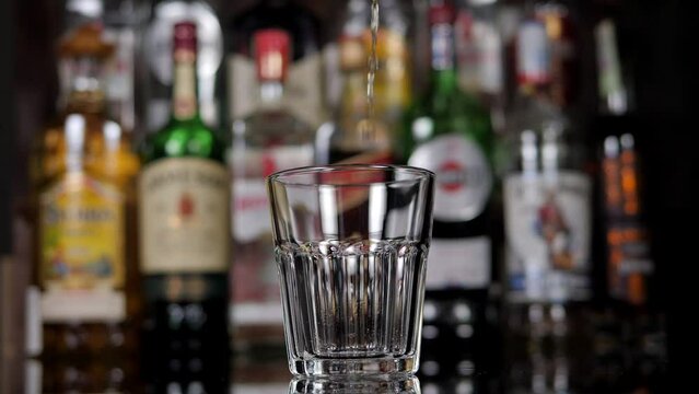 Close-up of a bartender pouring whiskey into a glass against the background of a bar with various bottles.