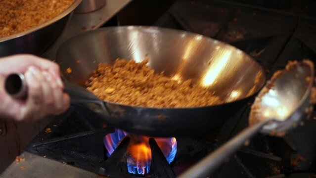 Chef flips and tosses fried rice in stainless wok over flaming fire in restaurant kitchen, slow motion close up 4K