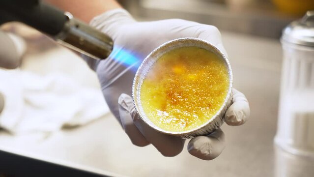 Chef uses kitchen hand torch to caramelize creme brulee top, close up slow motion 4K