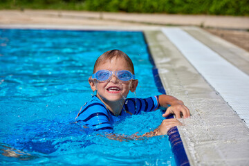 Happy little Caucasian boy swims and dives, has fun in the pool in protective glasses. Independent...