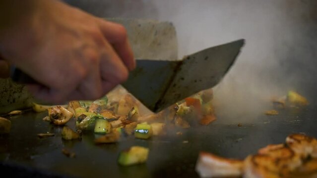 Chef sautes and flips mixed vegetables on hibachi grill top, close up slow motion 4K