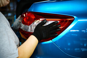 Worker installs tail light of new car in assembling workshop