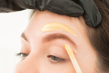 Young woman undergoing eyebrow correction procedure, waxing, wax depilation of eyebrow hair, brow...