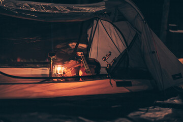 A gas lamp is on the tent floor at night and a bag with a ukulele and shoes next to it. Camping...