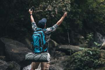 Hikers standing on the rock and raising hands to happy  with backpacks and background waterfall in the forest. hiking and adventure concept.