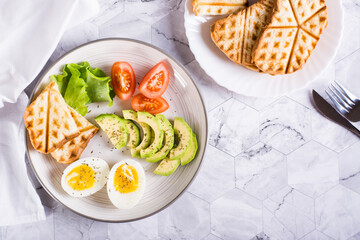 Sliced avocado, soft boiled egg, tomatoes and toast on a plate. Homemade breakfast. Top view