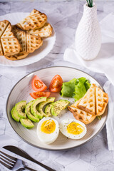 Avocado, soft boiled egg, tomatoes, lettuce and toast on a plate. Healthy food. Vertical view