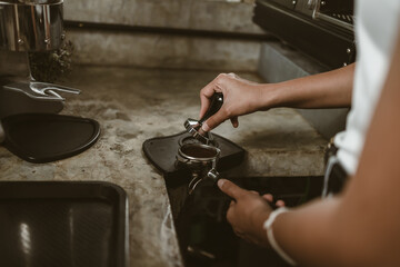 Barista using a tamper to press ground coffee into a portafilter. Coffee maker concept..