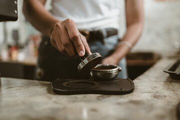 Barista using a tamper to press ground coffee into a portafilter. Coffee maker concept..
