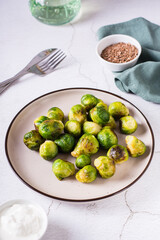 Homemade roasted Brussels sprouts on a plate and sauce in a bowl on the table. Vertical view