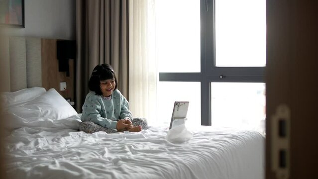 child with touchpad talking through video-chat while sitting on bed.
