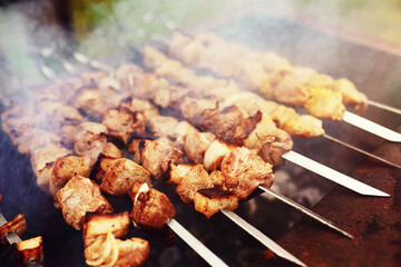 Selective focus. Cooking barbecue on the mangal in nature. Grilled tasty meet cooking on the party. Traditional Russian shashlik on a barbecue skewer on sunny forest.