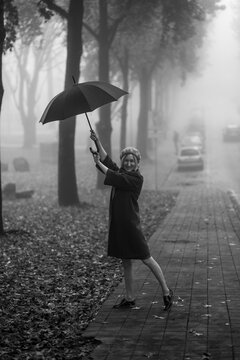 Woman having fun with an umbrella outside in foggy weather. Black and white photo.
