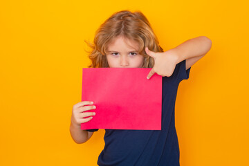 Fototapeta na wymiar Kid pointing on empty sheet of paper, isolated on yellow background. Portrait of a kid holding a blank placard, poster. Copy space.