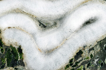 Top view of wastewater with air bubbles and moss flowing through a cracked ditch. Oxygen bubble in...