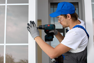 Professional installer of plastic windows stands in a doorway with a screwdriver doing the job. An...