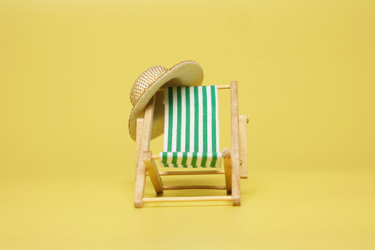 A picture of beach folding chair and straw hat on yellow background. Retirement and holiday concept