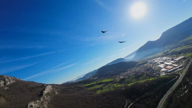 Birds flying in slow motion over the mountain, with the blue sky and the sun in the background. Image taken with a first-person drone. Image for action videos but also cinematic.
