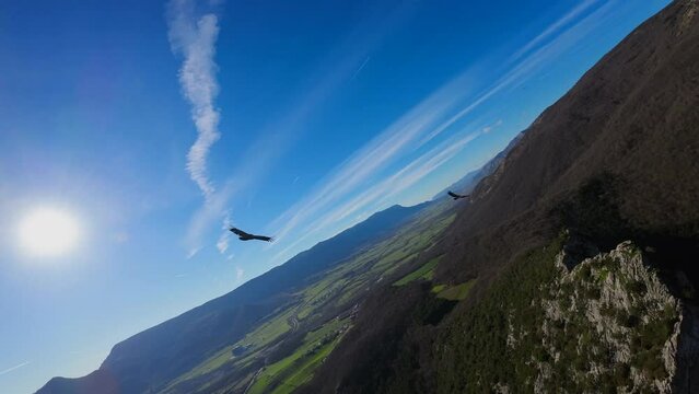First-person drone flight following birds close up at the top of a mountain, passing in front of the radiant sun and a blue sky. Impressive.