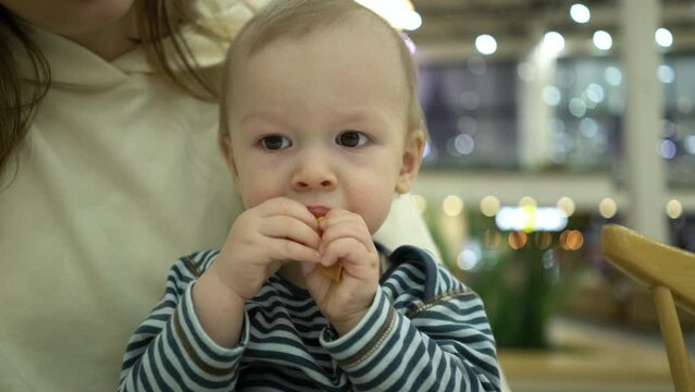 The son sits in his mother's arms and eats a slice of dried mango.
