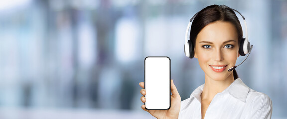 Customer support phone operator in headset holding showing smartphone cell phone mobile white blank mock up screen, on blurred office background. Consulting and assistance service call center ad.