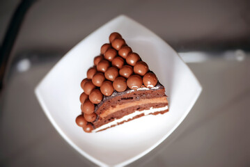 Chocolate birthday cake. Cake decorated with Maltesers chocolate balls. Chocolate cake on a stand. Chocolate cake with your own hands. Homemade chocolate cake. Cutaway cake. A piece of cake on a plate