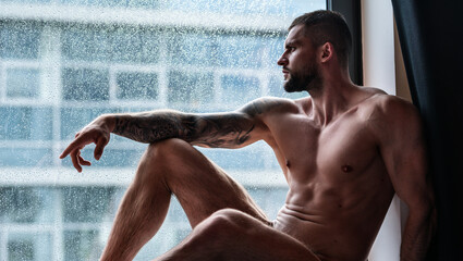 Handsome muscular man in bedroom on window curtains. Young handsome sexy man resting at home. Guy with athletic muscles. Sexy young handsome naked man on bedroom. Seductive gay.