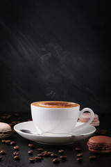 Coffee with macaroon and a spoon on a black background. White cup with cappuccino, coffee beans on a dark background. breakfast on a black background, coffee beans.