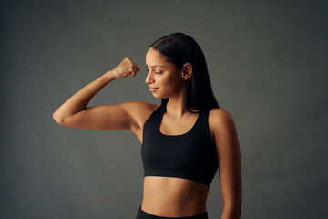Fototapeta na wymiar Young biracial woman wearing sports bra flexing bicep in studio